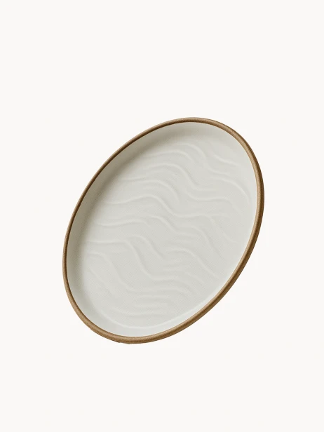 Ceramiczny talerz o matowym wykończeniu w odcieniu złamanej bieli, ozdobiony strukturalnym wzorem przypominającym wydmy piaskowe i wykończony naturalnym brązowym rantem.